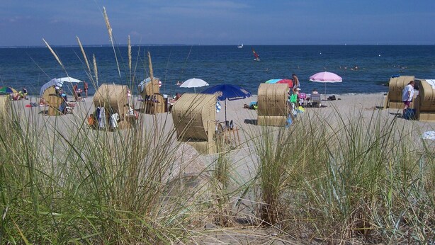 Una playa con cabañas playeras, sombrillas y gente disfrutando del mar.