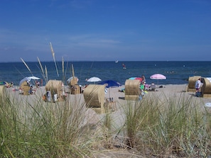 Une plage avec des cabanes, des parasols et des gens qui profitent de la mer.