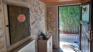 A stone wall with a radiator, a door with a plaque, and a view of greenery outside.