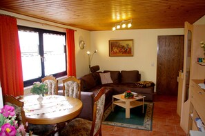 Un salon chaleureux avec un plafond en bois, une table à manger avec des chaises, un canapé et une petite table basse.