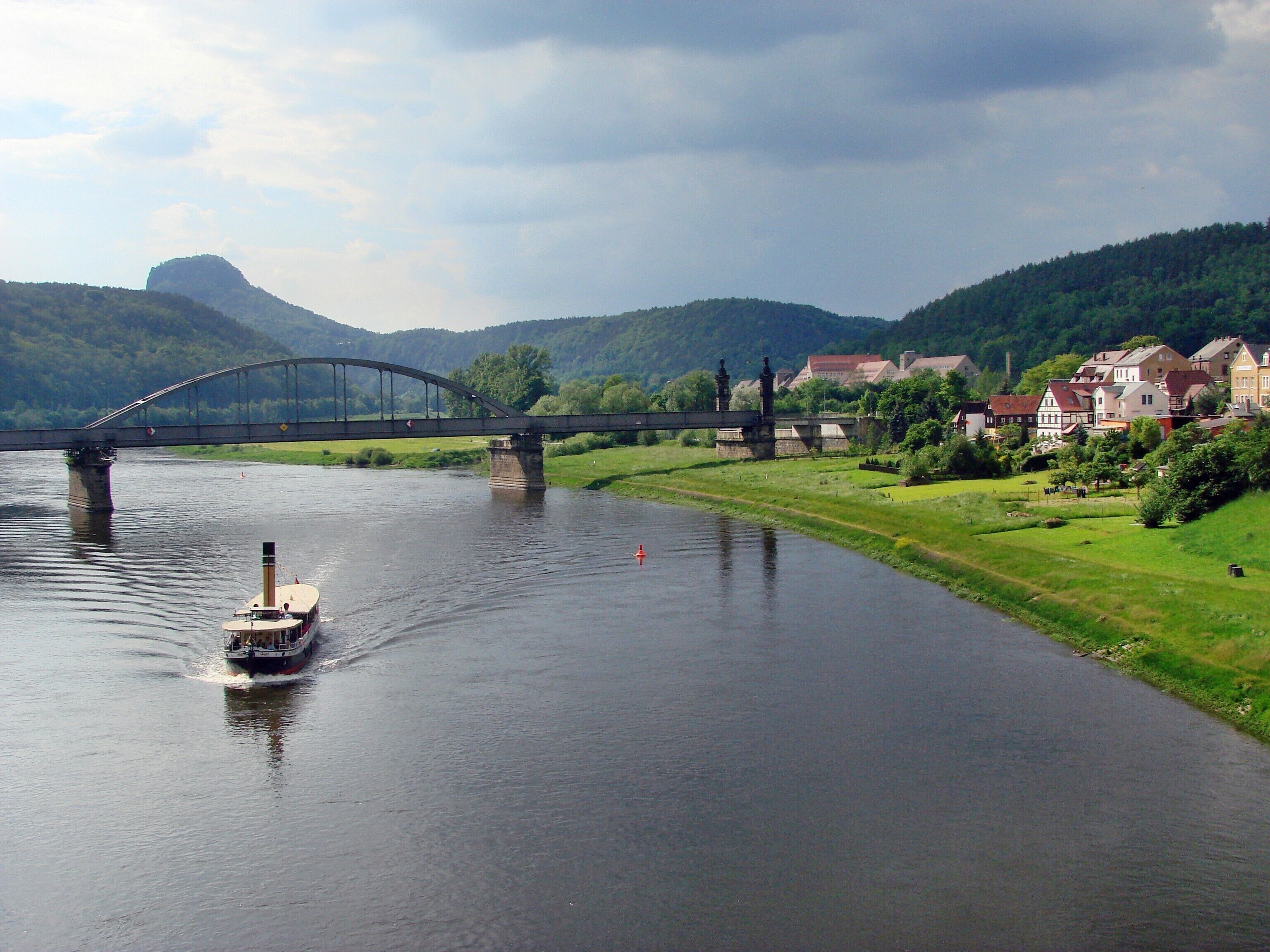 A river with a boat, a bridge, and houses in the background.