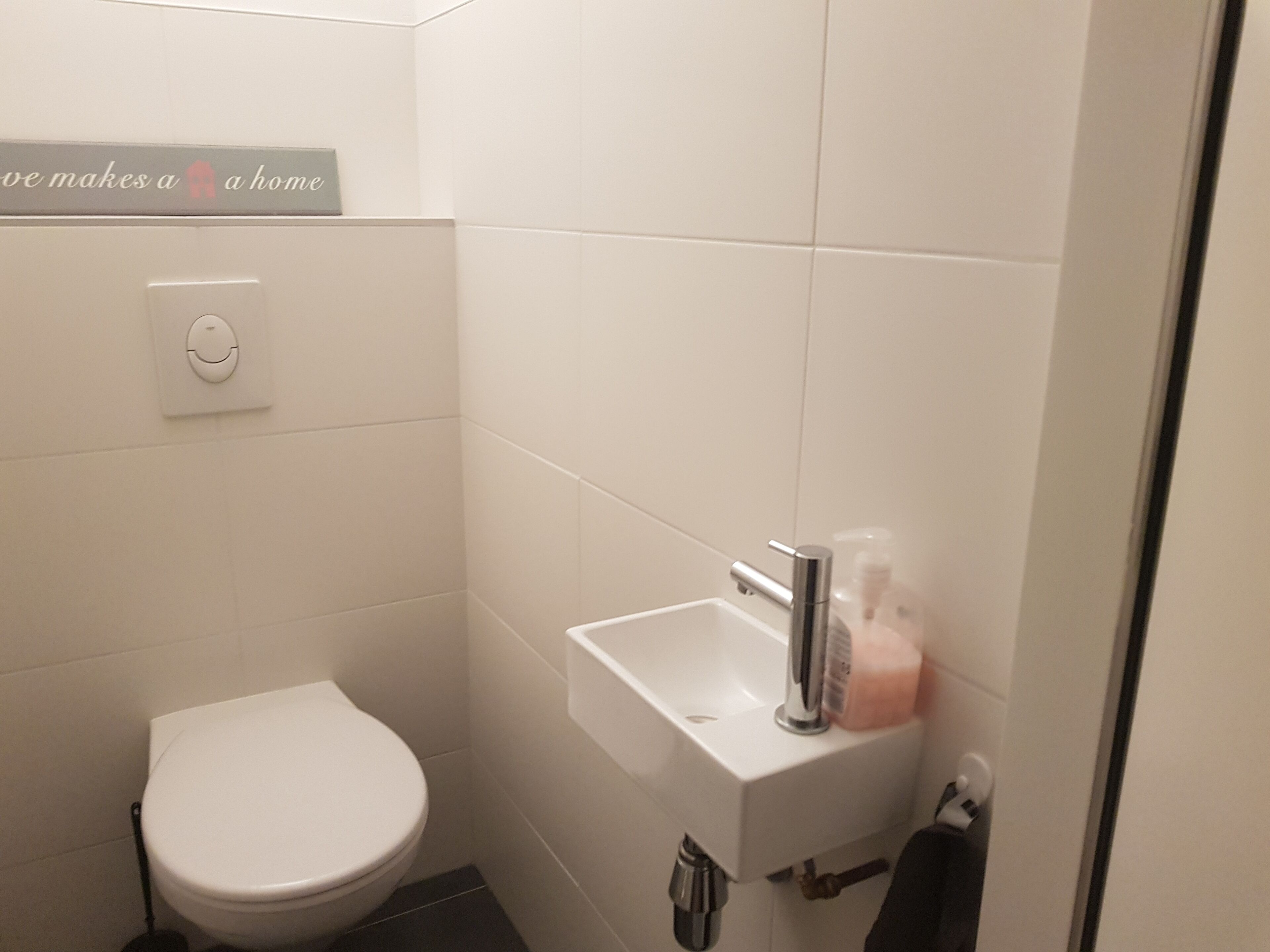 Une petite salle de bain blanche, équipée de toilettes, d’un lavabo et d’un distributeur de savon.