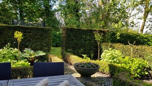 A wooden table with two stone sculptures, surrounded by lush greenery and a stone pathway.