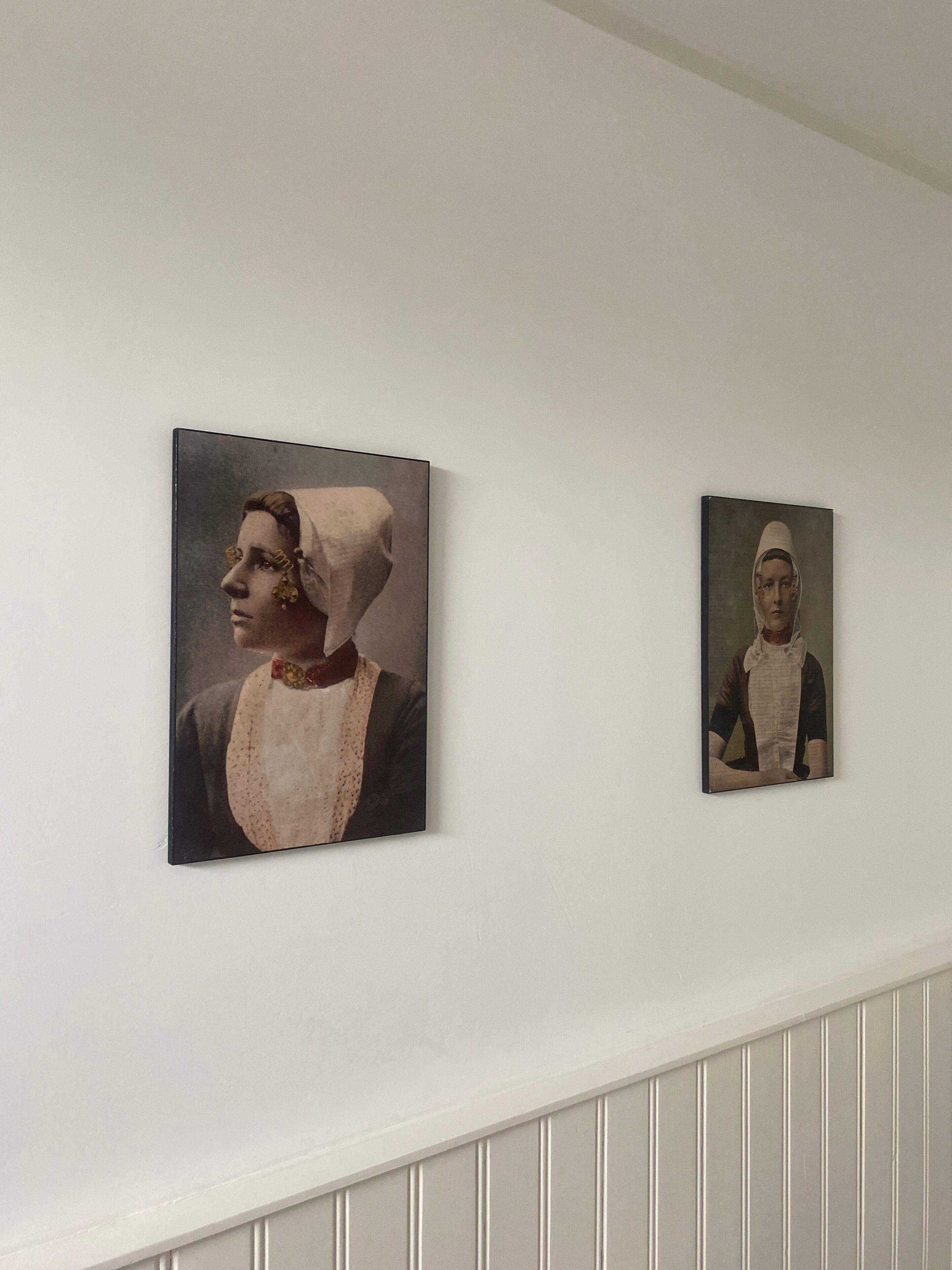 Twee ingelijste portretten van personen aan een witte muur.