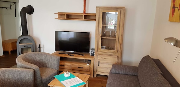 Una sala de estar con televisor, sofá, sillón, aparador de madera y chimenea.