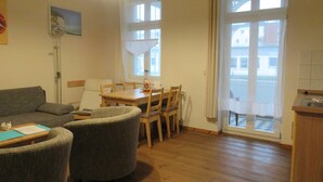 A living room with a sofa, armchairs, a dining table with chairs, a floor lamp, and a view through a large window. - Jasmund - Pension Waldrose (Sellin)