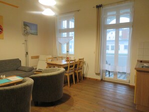 Una sala de estar con sofá, sillones, una mesa de comedor con sillas, una lámpara de pie y vistas a través de un ventanal.