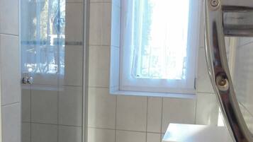 Ein Badezimmer mit Dusche, Fenster und einem weißen Schrank.
