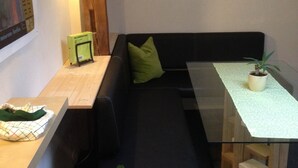 A modern, compact living space with a glass-top table, a black sofa with a green pillow, and a wooden bench. - Details about our apartment. (Berlin)