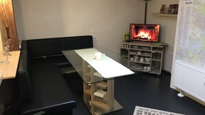 A cozy living room with a glass-top table, a black sofa, a fireplace, a map on the wall, and a shelf with books and decorative items. - Details about our apartment. (Berlin)