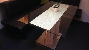 A modern dining area with a glass-top table, a potted plant, and a green cushion on a black sofa. - Details about our apartment. (Berlin)