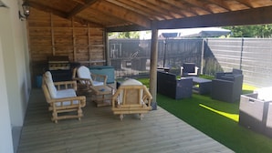 Un patio al aire libre con mobiliario de madera, una parrilla y un área cercada con césped artificial.