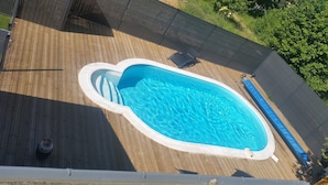 Vista aérea de una piscina con cubierta de madera, rodeada por una valla y follaje.