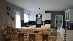Una cocina con una isla de piedra, taburetes de bar y armarios blancos.