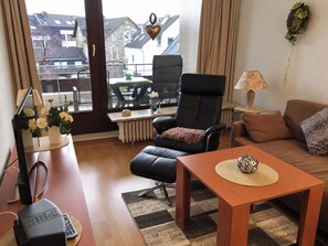 Een gemeubileerde woonkamer met een zwarte leren fauteuil, een bruine bank, een houten salontafel en uitzicht buiten door een groot raam.