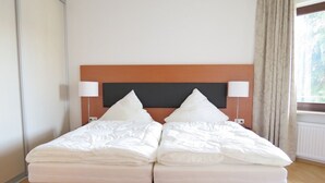 Una cama doble con cabecera de madera, dos lámparas de noche y una ventana con cortinas.