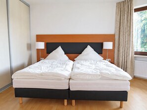 A double bed with a wooden headboard, two bedside lamps, and a window with curtains.