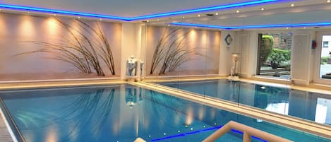 Una amplia piscina cubierta con agua cristalina, rodeada de paredes con plantas decorativas y un moderno diseño de techo.
