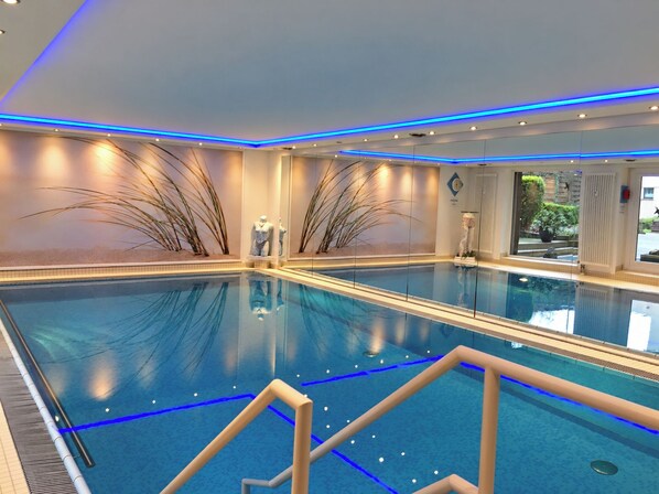 A large indoor swimming pool with clear blue water, surrounded by walls with decorative plants and a modern ceiling design.