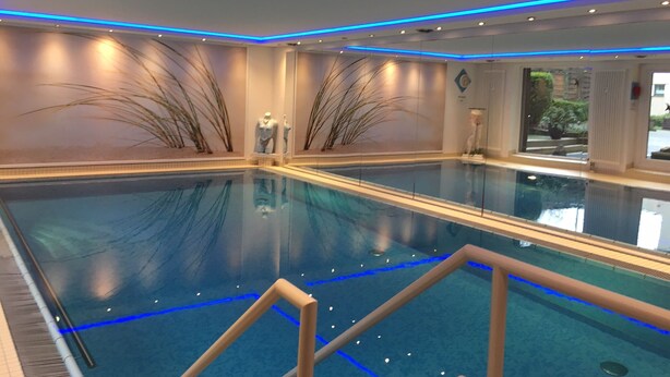 Una amplia piscina interior con iluminación LED azul a lo largo del techo, rodeada de paredes con arreglos decorativos de plantas.