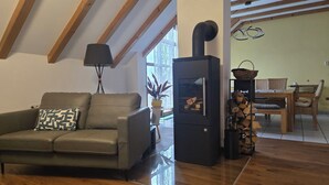Ein gemütliches Wohnzimmer mit einer Couch, einem schwarzen Kaminofen und einem Essbereich mit Tisch und Stühlen.