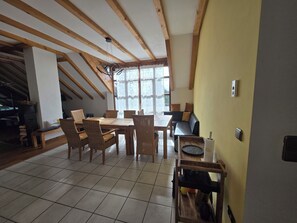 Un comedor con una mesa y sillas de madera, un sofá y una ventana con cortinas de encaje.