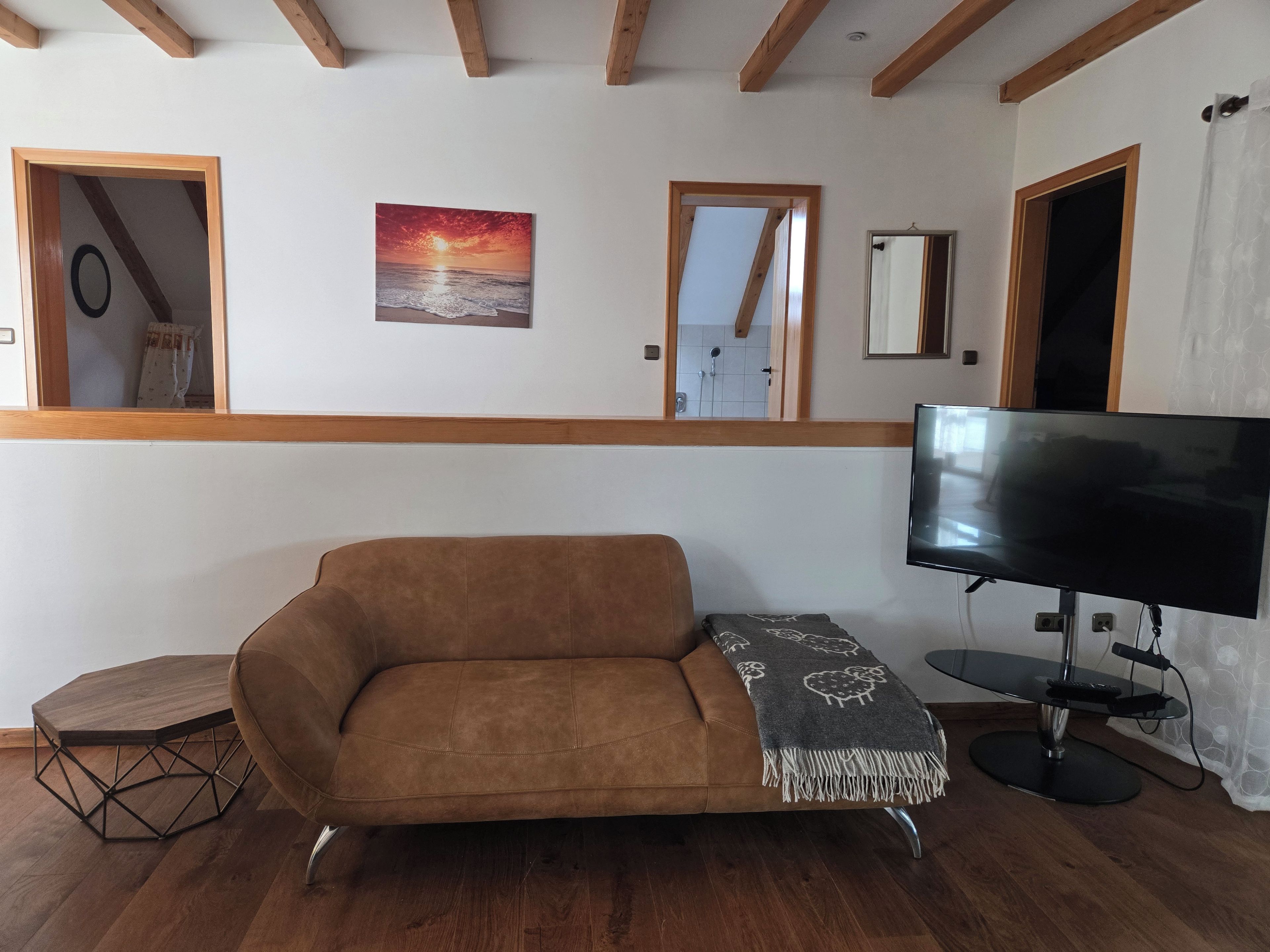 Un salon avec un canapé marron, un téléviseur et un tableau représentant un coucher de soleil.