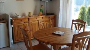 A wooden dining table with chairs, a television on a stand, and a window with curtains. - Charming apartment in chalet, close to ski slopes and town center    (Gérardmer)