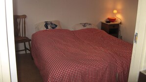Un dormitorio con una colcha a cuadros, una silla, una mesita de noche con una lámpara y una pared con un cartel.