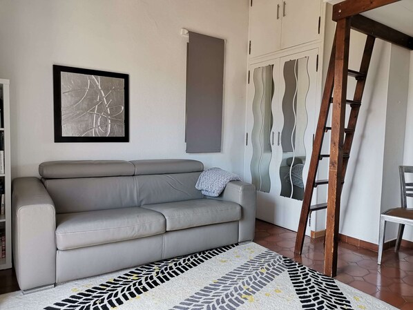 A living room with a grey sofa, a patterned rug, a framed abstract artwork, a wardrobe with a unique design, and a wooden ladder. - Outstanding rental property with pool for 8 persons i cassis france (Cassis)