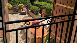 A balcony with a stone floor, a wooden table with chairs, and a view of the sea and a mountain.