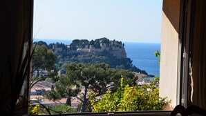 A view from a window overlooking a coastal town with a prominent castle on a cliff, surrounded by trees and buildings.
