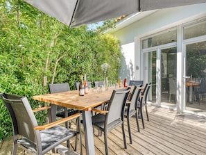 Zona pranzo all'aperto con tavolo e sedie in legno, circondata dal verde.