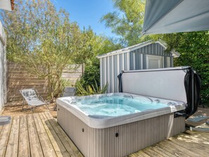 Ein Whirlpool auf einer Holzdiele mit überdachtem Bereich und einem Schuppen im Hintergrund.