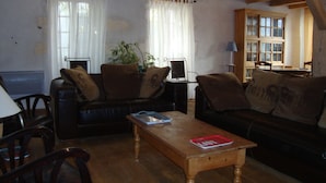 Una sala de estar acogedora con techo de madera, un sofá de cuero negro, una mesa de centro de madera y un comedor con mesa y sillas.