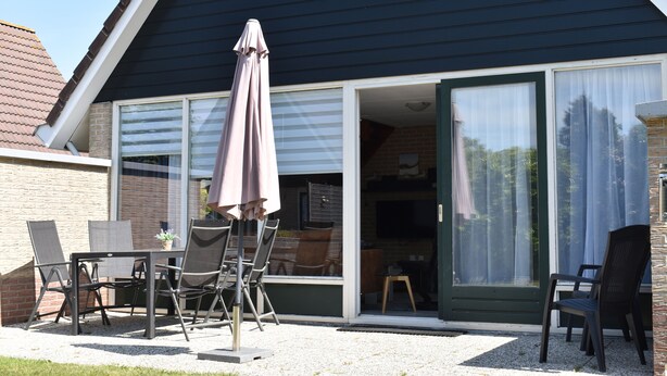 A house with a patio area featuring a table and chairs, an umbrella, and a sliding glass door leading to an interior space. - Comfortable holiday home near the beach with garden, with playground and pool (Sint Maarten)