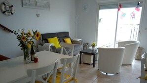 A dining area with a white table and chairs, a sofa with yellow cushions, and a window with flags.