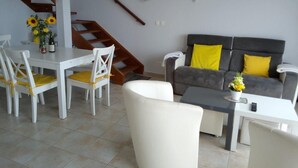 A living room with a dining table, chairs, a sofa, and a staircase.