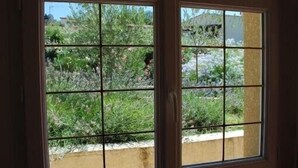 Una porta con finestra a griglia, che dà su un'area giardino con diverse piante e una recinzione visibile.