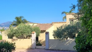 Un edificio residenziale con tetto in tegole, un cancello e vegetazione circostante.