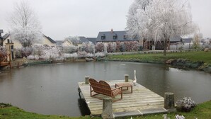 A pond with a wooden dock and chairs, surrounded by snow-covered trees and houses. - The charm of the countryside to the city (Barentin)