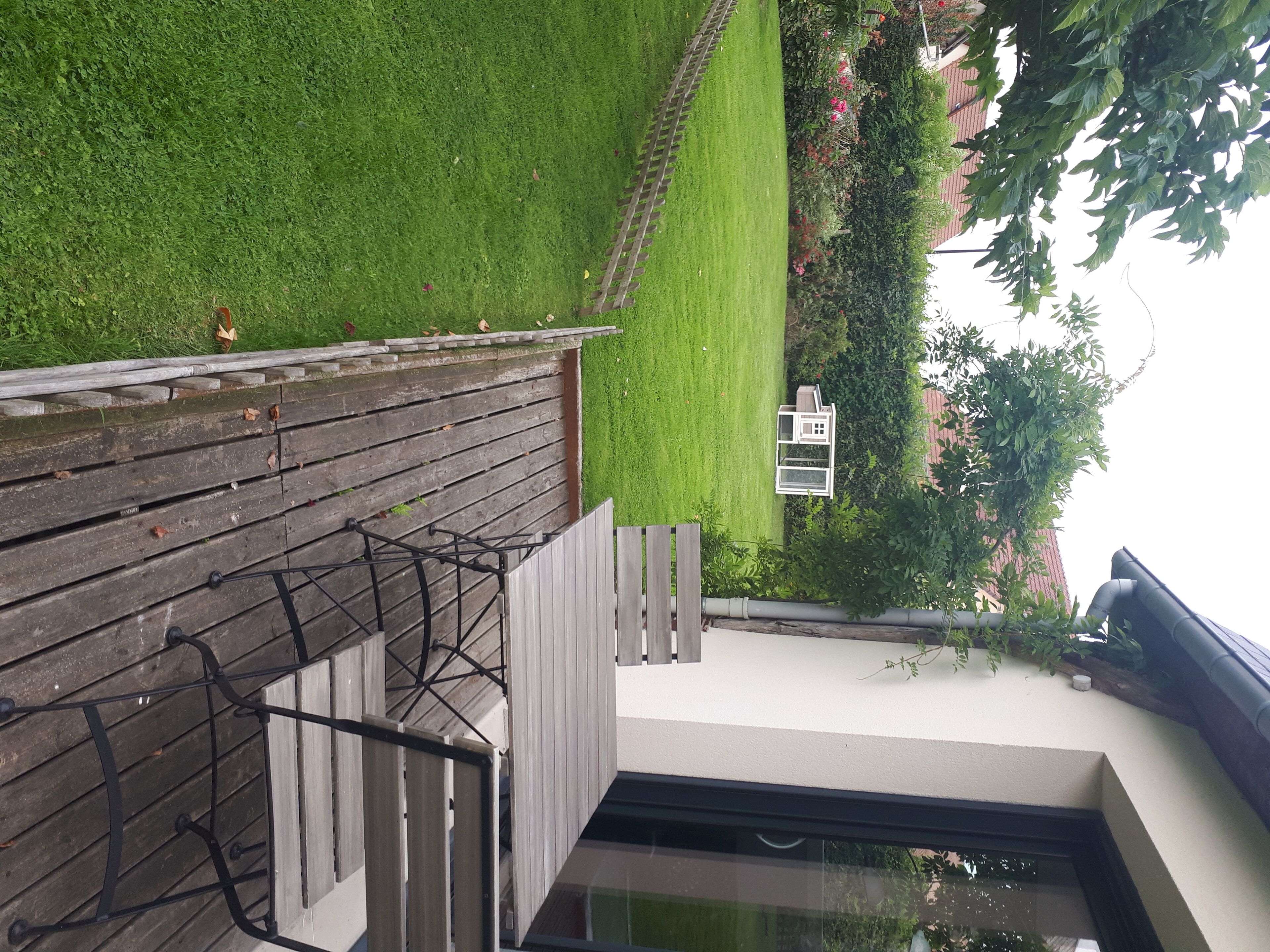 Eine moderne Terrasse im Freien mit Holzgeländer, einem kleinen weißen Tisch und einer Glastür, die auf einen Balkon führt.