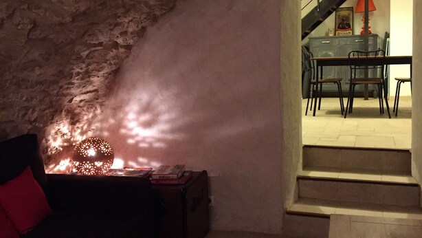 An underground room with a stone wall, a table with chairs, a sofa, and a lamp.
