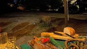 An outdoor dining area with a table set for a meal, a basket, and a glass of water.