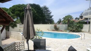 Un espace piscine doté d’un sol en pierre, d’un coin salon abrité et d’un escalier pour accéder à la piscine.