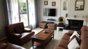 Un salon avec des canapés en cuir, une table basse en bois, un téléviseur à écran plat, une cheminée et un balcon agrémenté de rideaux.
