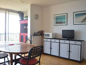 Um espaço de estar compacto com mesa de jantar, cadeiras, cozinha compacta equipada com micro-ondas, televisão e pequeno armário. Há uma janela com vista para o exterior.