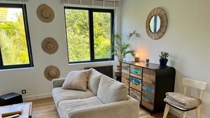 A cozy room with a striped sofa, a wooden cabinet with drawers, a white chair, and a large window with a view of greenery. - House seafront, very quiet hamlet (Vicq-Sur-Mer)