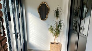 A hallway with a wooden floor, a potted plant, a mirror, and a door with blinds. - House seafront, very quiet hamlet (Vicq-Sur-Mer)