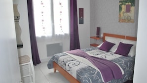 A bedroom with a bed, a nightstand, a chair, and a window with curtains.